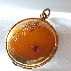 Peut inclure: Un médaillon en or avec un motif de rose et de fer à cheval. Le médaillon a une pierre rouge au centre.