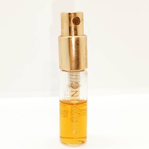 May include: A small, clear glass bottle with a gold cap and a gold label that reads "JASMINE  MAC + HUM  COLLECTION  1.0 OZ  100%  PERFUME OIL". The bottle is filled with a light amber liquid.