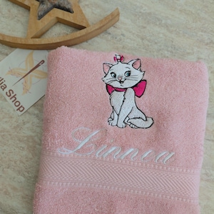 Può includere: Un asciugamano in spugna rosa chiaro con il ricamo di un gatto bianco che indossa un fiocco rosa acceso sulla testa e sul collo. Sotto il gatto, il nome Linnea è ricamato in corsivo bianco. L'asciugamano presenta un bordo testurizzato.