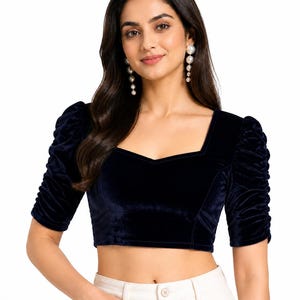 May include: A dark navy blue velvet crop top featuring a square neckline and elbow-length sleeves with gathered, ruched detailing. The fitted bodice is constructed from a soft, plush fabric, providing a structured silhouette with a clean, straight hemline.