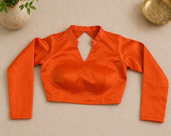 Puede incluir: Blusa naranja brillante de manga larga con cuello mandarín y escote en V. La blusa está confeccionada con una tela suave y brillante. La prenda se muestra sobre un fondo neutro.