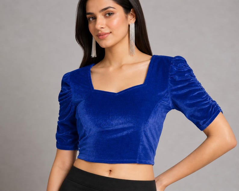 May include: A royal blue velvet crop top featuring a square neckline and short sleeves with gathered, ruched detailing. The garment is constructed from a soft, textured fabric and has a fitted silhouette that ends above the waistline.