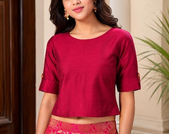 Puede incluir: Una blusa de manga corta en color magenta intenso con cuello redondo y mangas con vuelta adornadas con pequeños botones dorados. La prenda se combina con una falda rosa brillante que presenta un patrón floral dorado tejido en la tela.