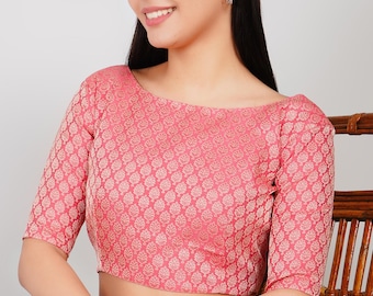 Puede incluir: Una blusa rosa con cuello barco y mangas cortas. La tela presenta un patrón repetido de pequeñas formas de hojas de color claro. La blusa se combina con pantalones rojos, creando un contraste de color.
