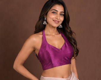 Puede incluir: Un top halter de color magenta vibrante con escote en V y un diseño estructurado sin mangas. La prenda está confeccionada con una tela suave y ligeramente texturizada que llega a la cintura, combinada con pendientes jhumka plateados.