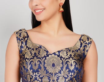 Puede incluir: Top sin mangas azul marino con un estampado de brocado floral dorado. El top tiene un escote amplio y redondo. La modelo lleva pendientes rojos y dorados.