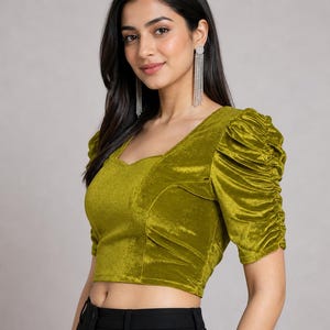 May include: A chartreuse velvet crop top featuring a sweetheart neckline and short, puffed sleeves with gathered detailing. The fabric has a soft, reflective sheen, and the garment is fitted through the bodice with structured seams.