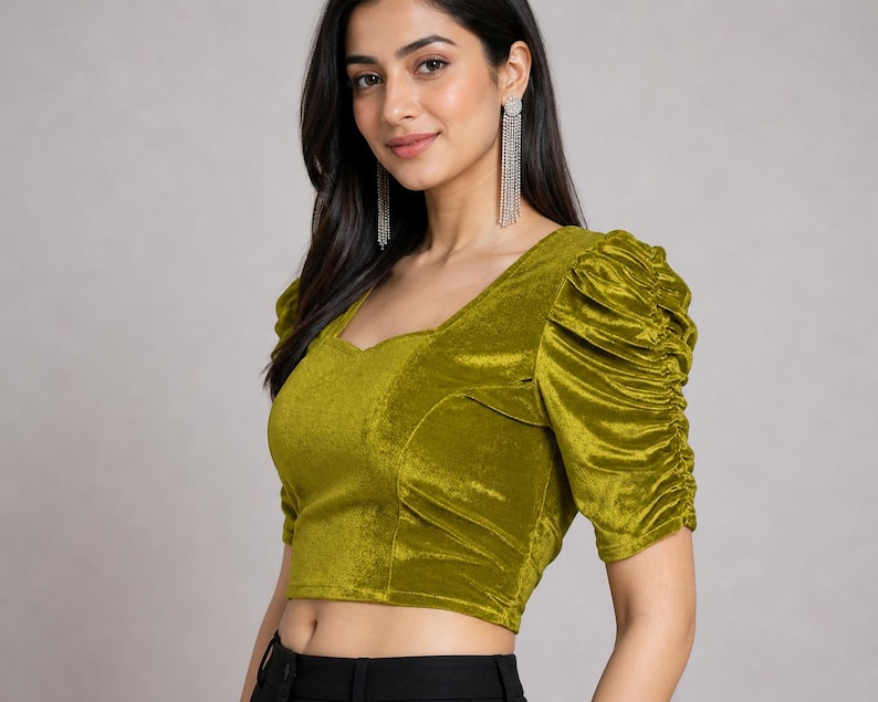 May include: A chartreuse velvet crop top featuring a sweetheart neckline and short, puffed sleeves with gathered detailing. The fabric has a soft, reflective sheen, and the garment is fitted through the bodice with structured seams.