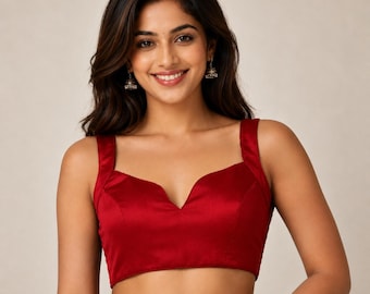 Puede incluir: Una blusa sin mangas de satén rojo intenso con escote corazón y tirantes anchos. La prenda está confeccionada con un tejido liso y brillante que proporciona un color sólido y uniforme en todo el diseño del corpiño delantero.