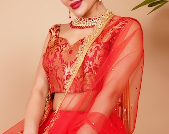 Puede incluir: Una mujer con un atuendo tradicional indio rojo y dorado. El atuendo incluye una blusa roja con bordados dorados, una falda a juego y un velo rojo transparente. También lleva un collar, pendientes y una diadema rojos y dorados.