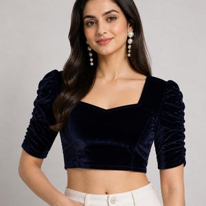 May include: A dark navy blue velvet crop top featuring a square neckline and elbow-length sleeves with gathered, ruched detailing. The fitted garment has a structured bodice design and a smooth, soft-textured finish throughout the fabric.