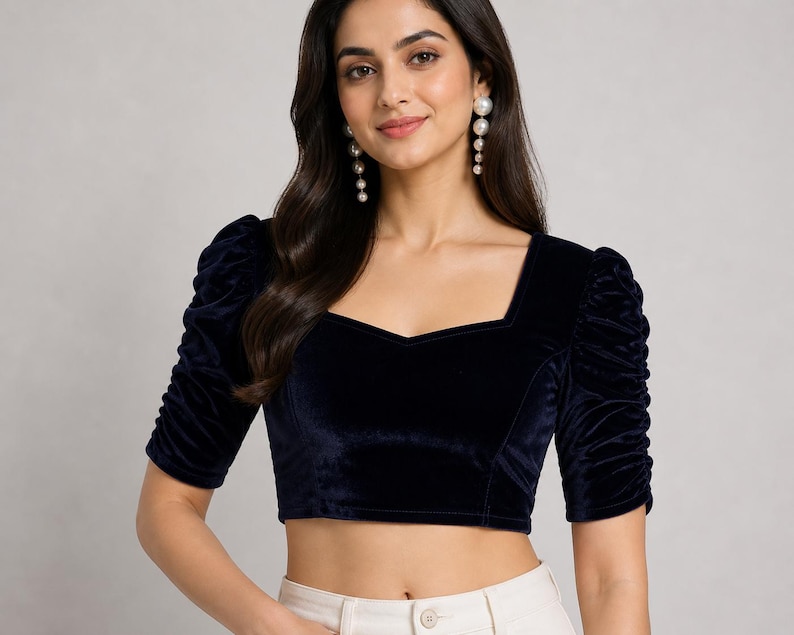 May include: A dark navy blue velvet crop top featuring a square neckline and elbow-length sleeves with gathered, ruched detailing. The fitted garment has a structured bodice design and a smooth, soft-textured finish throughout the fabric.