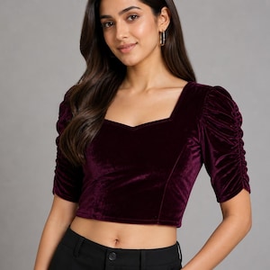 May include: A deep burgundy velvet crop top featuring a square neckline and short, ruched puff sleeves. The garment is constructed from a soft, plush fabric with a subtle sheen, designed with a fitted silhouette that ends above the waistline.
