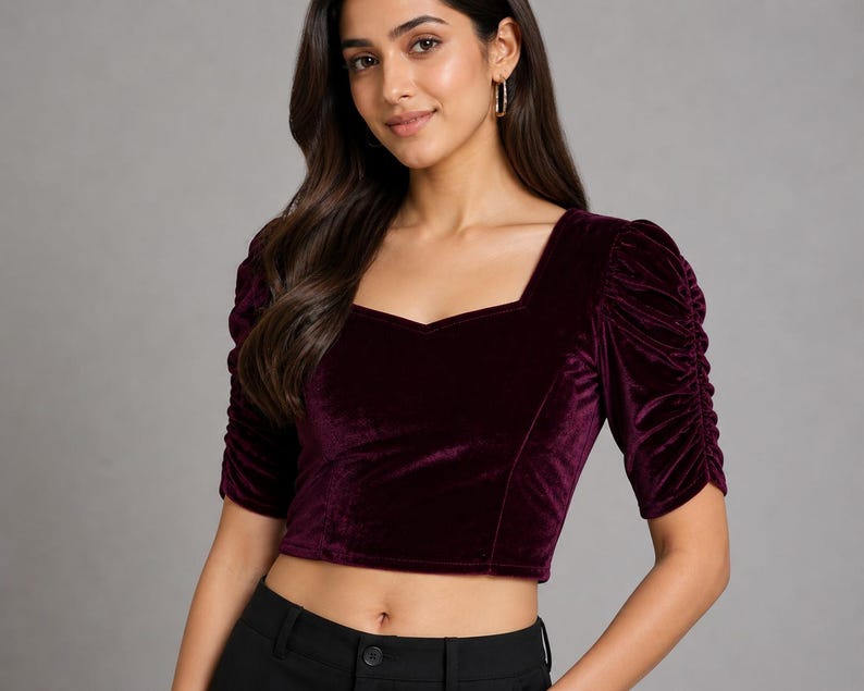 May include: A deep burgundy velvet crop top featuring a square neckline and short, ruched puff sleeves. The garment is constructed from a soft, plush fabric with a subtle sheen, designed with a fitted silhouette that ends above the waistline.