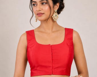 Puede incluir: Una blusa roja sin mangas con cuello cuadrado y una serie de pequeños botones en el centro. La blusa está hecha de una tela lisa y sólida. La modelo lleva pendientes dorados con detalles verdes.