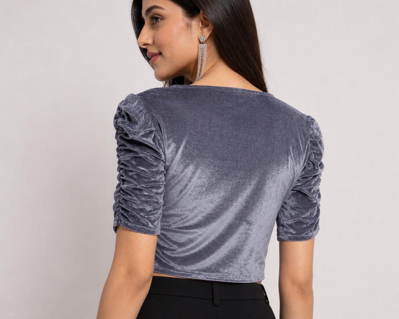 May include: A grey velvet top featuring short sleeves with gathered, ruched detailing along the shoulders and arms. The garment has a V-neckline and a cropped length, constructed from a soft, light-reflecting fabric with a smooth, plush texture.