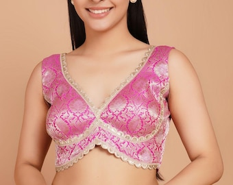 Puede incluir: Una blusa sin mangas en tela de brocado fucsia vibrante y oro metálico. La prenda presenta un escote en V profundo con ribete dorado festoneado en los bordes y un dobladillo corto, mostrando un patrón detallado de flores y hojas.
