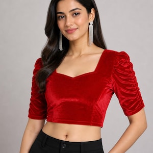 May include: A vibrant red velvet crop top featuring a square neckline and elbow-length sleeves with gathered, ruched detailing. The fitted garment has a clean, straight hemline and a soft, textured finish, providing a structured look.