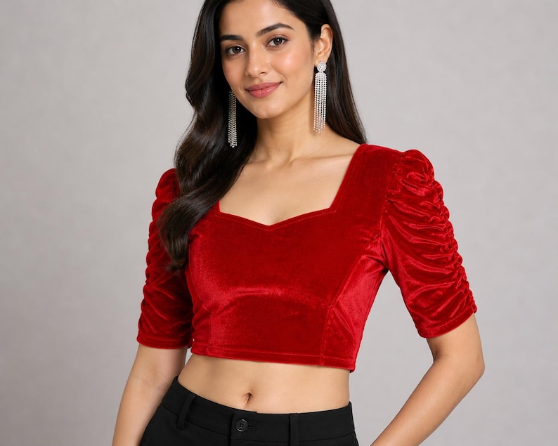 May include: A vibrant red velvet crop top featuring a square neckline and elbow-length sleeves with gathered, ruched detailing. The fitted garment has a clean, straight hemline and a soft, textured finish, providing a structured look.