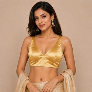 May include: A sleeveless gold satin blouse featuring a deep V-neckline and a cropped silhouette. The garment is constructed with structured seams along the bodice, providing a fitted appearance. The fabric has a smooth, reflective finish.
