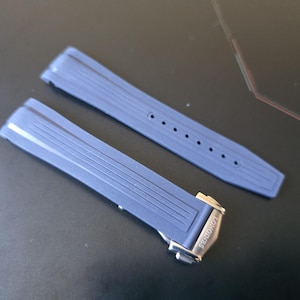 May include: Two blue watch straps with a ridged design. One strap has a silver clasp with the brand name "LONGINES" engraved. The straps are made of a flexible material and have several holes for adjustment.
