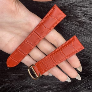 Puede incluir: Dos correas de reloj de cuero rojo con un patr&oacute;n de cocodrilo. Una correa tiene una hebilla dorada.