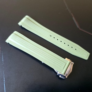 May include: Two light green watch straps with a silver clasp. The straps have a ribbed design and are made of a flexible material. The clasp is engraved with the brand name "Longines".