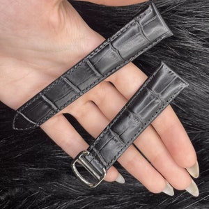 Puede incluir: Dos correas de reloj de cuero negro con estampado de cocodrilo. La correa de la izquierda tiene una hebilla plateada.