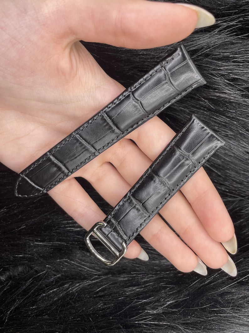 Puede incluir: Dos correas de reloj de cuero negro con estampado de cocodrilo. La correa de la izquierda tiene una hebilla plateada.