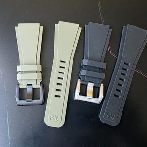 May include: Four watch straps in shades of green and black. Two are light green with black buckles, and two are black with silver buckles. Each strap has the letters "BR" printed on it.