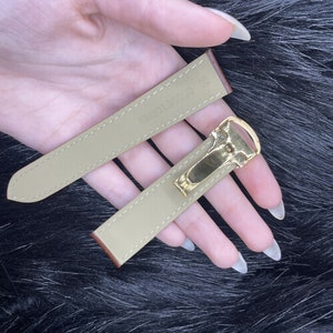 Puede incluir: Dos correas de reloj de cuero beige con herrajes dorados. La correa m&aacute;s larga tiene el texto "CARRETER" impreso.