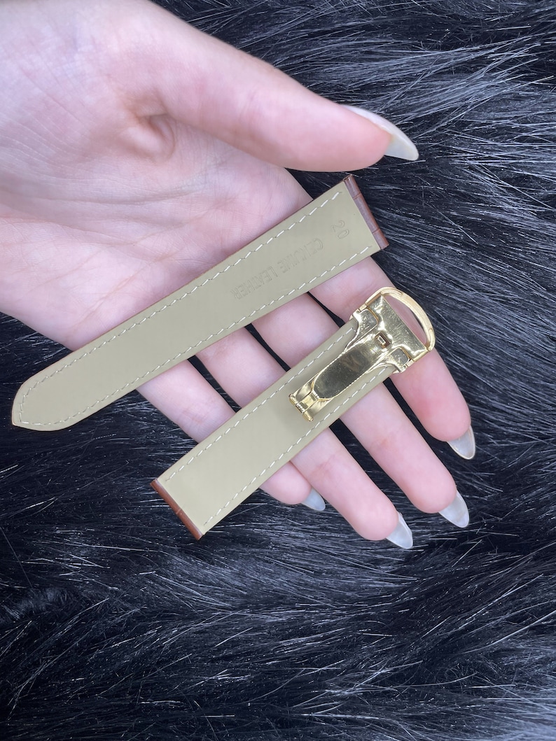 Puede incluir: Dos correas de reloj de cuero beige con herrajes dorados. La correa m&aacute;s larga tiene el texto "CARRETER" impreso.