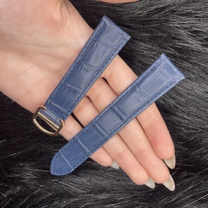 Puede incluir: Dos correas de reloj de cuero azul con estampado de cocodrilo. Una correa tiene una hebilla dorada.