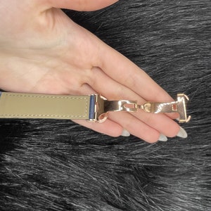 Puede incluir: Un cierre de correa de reloj dorado con una correa de cuero beige. El cierre tiene un acabado pulido y est&aacute; dise&ntilde;ado para asegurar la correa del reloj.