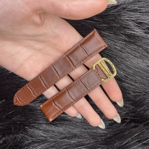 Puede incluir: Dos correas de reloj de cuero marr&oacute;n con una hebilla dorada. Las correas tienen un patr&oacute;n de cocodrilo.