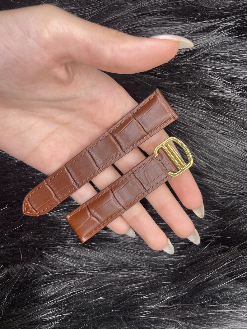 Puede incluir: Dos correas de reloj de cuero marr&oacute;n con una hebilla dorada. Las correas tienen un patr&oacute;n de cocodrilo.