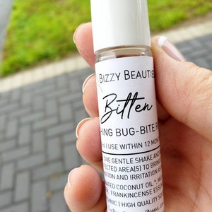May include: A white roll-on bottle with a black label that reads "Bizzy Beautie Bitten HING BUG-BITE REMEDY" and instructions for use. The bottle is being held in a hand.