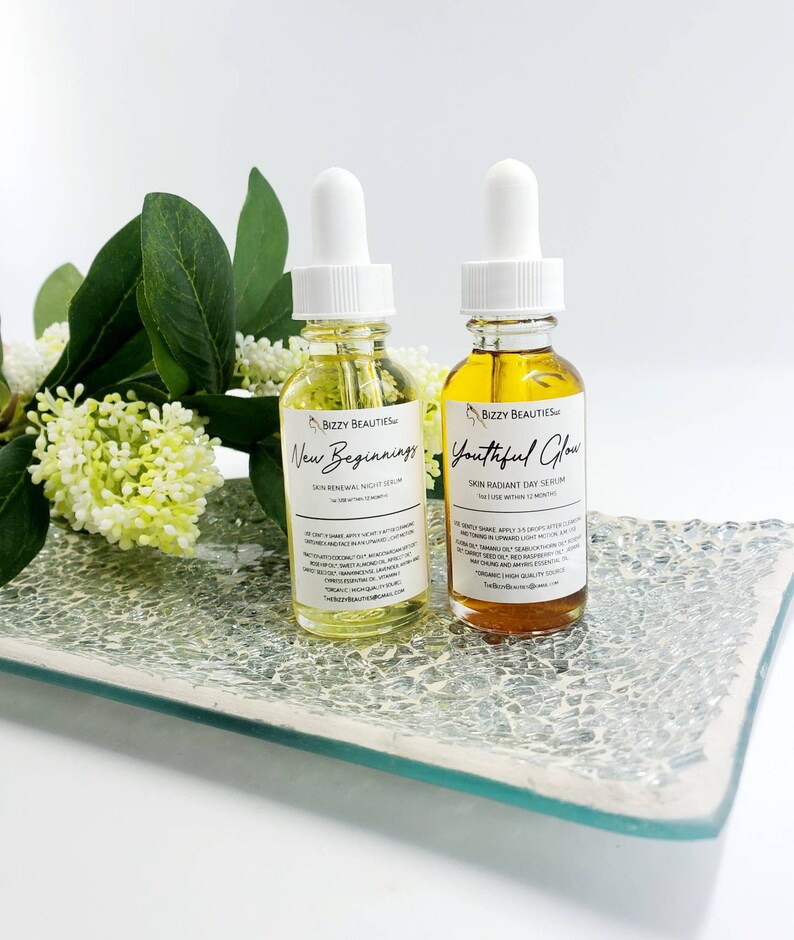 May include: Two amber glass bottles with dropper tops, labeled "Bizzy Beauties" and containing facial serums. The bottles are labeled "New Beginnings Skin Renewal Night Serum" and "Youthful Glow Skin Radiant Day Serum".