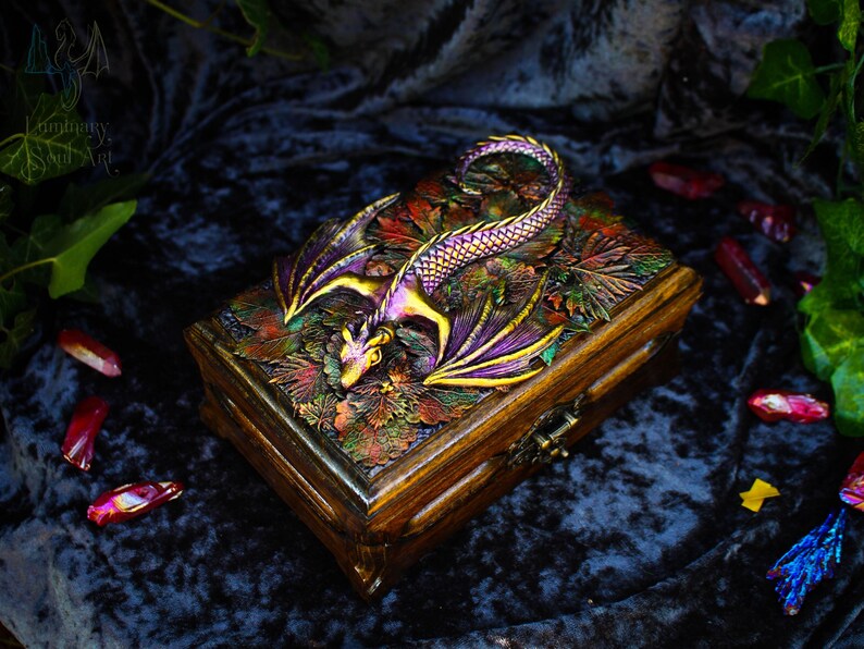 May include: A wooden box with a dragon design. The dragon is made of resin and is painted in shades of purple, gold, and green. The box is decorated with a variety of autumn leaves.