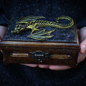 May include: A wooden box with a gold dragon design on the lid. The box has a carved design around the edges and a metal latch.