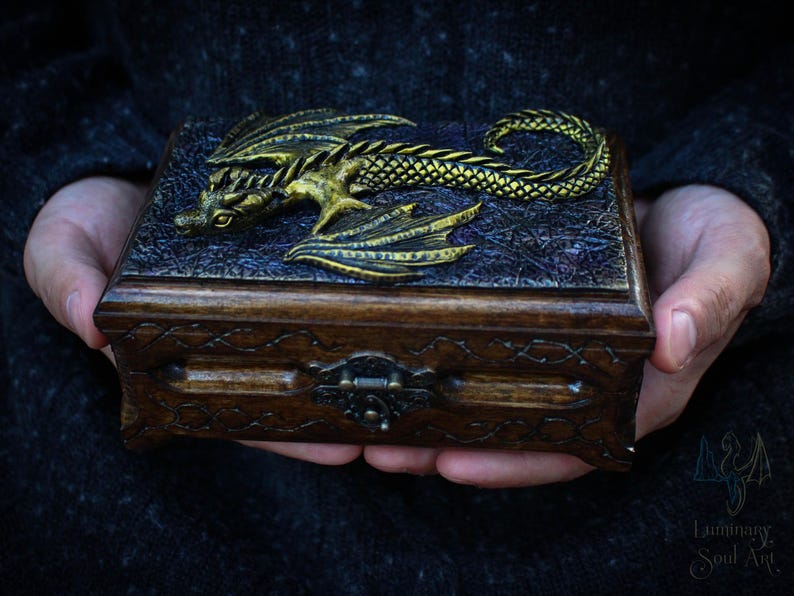 May include: A wooden box with a gold dragon design on the lid. The box has a carved design around the edges and a metal latch.