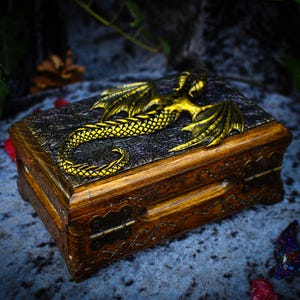 May include: A wooden box with a dragon design on the lid. The dragon is gold and has intricate details. The box has a hinged lid and a brass latch.