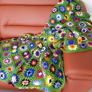 Könnte beinhalten: Eine grüne Häkeldecke mit bunten Blumenmustern. Die Decke liegt auf einem braunen Ledersofa.