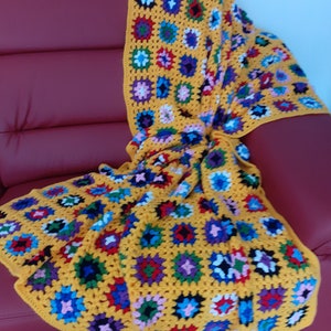 Peut inclure: Une couverture en crochet jaune avec un motif géométrique coloré. La couverture est faite de carrés de différentes couleurs et motifs, notamment rouge, bleu, vert, violet et blanc.
