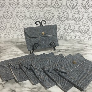 May include: A set of six small gray and white patterned fabric pouches with a single button closure. The pouches are stacked on top of each other.