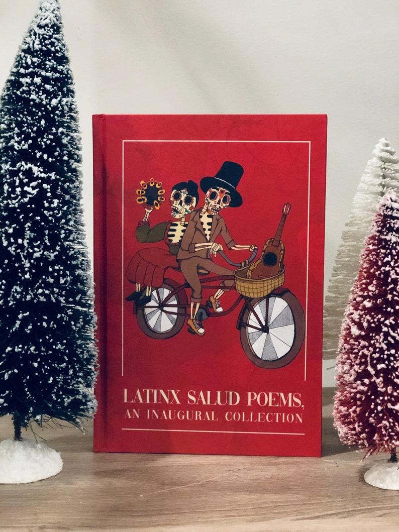 Peut inclure: Un livre reli&eacute; rouge avec le titre "Latinx Salud Poems, An Inaugural Collection" et une illustration de deux squelettes &agrave; v&eacute;lo. Les squelettes portent des chapeaux et l'un d'eux tient une guitare.