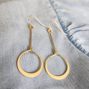May include: A pair of gold dangle earrings with a simple circle design. The earrings are made of wire and have a delicate, minimalist look.