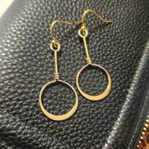 May include: A pair of gold-toned earrings with a simple circle design. The earrings are made of wire and have a dangling circle shape.
