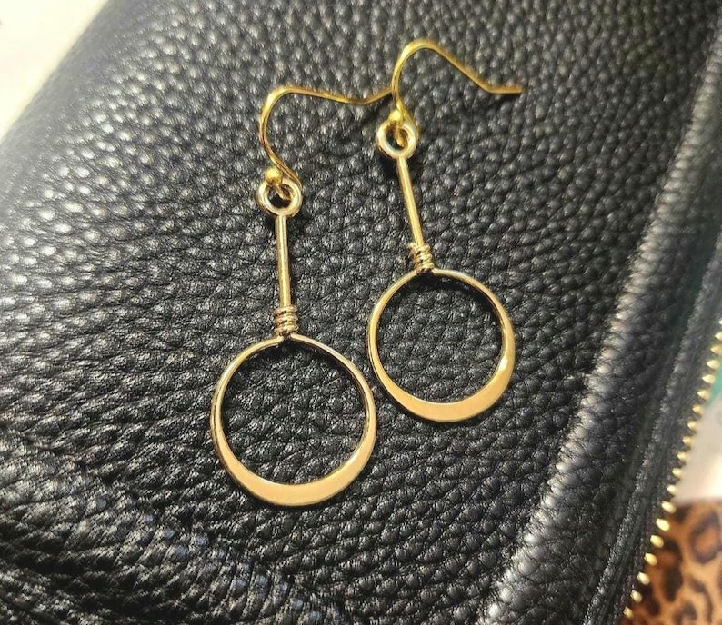 May include: A pair of gold-toned earrings with a simple circle design. The earrings are made of wire and have a dangling circle shape.
