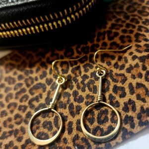 May include: A pair of gold hoop earrings with a simple, minimalist design. The hoops are suspended from a straight wire, creating a delicate and modern look.
